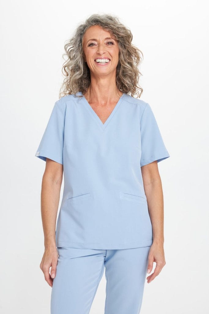 Kobieta w jasnoniebieskim komplecie odzieży medycznej uśmiecha się.