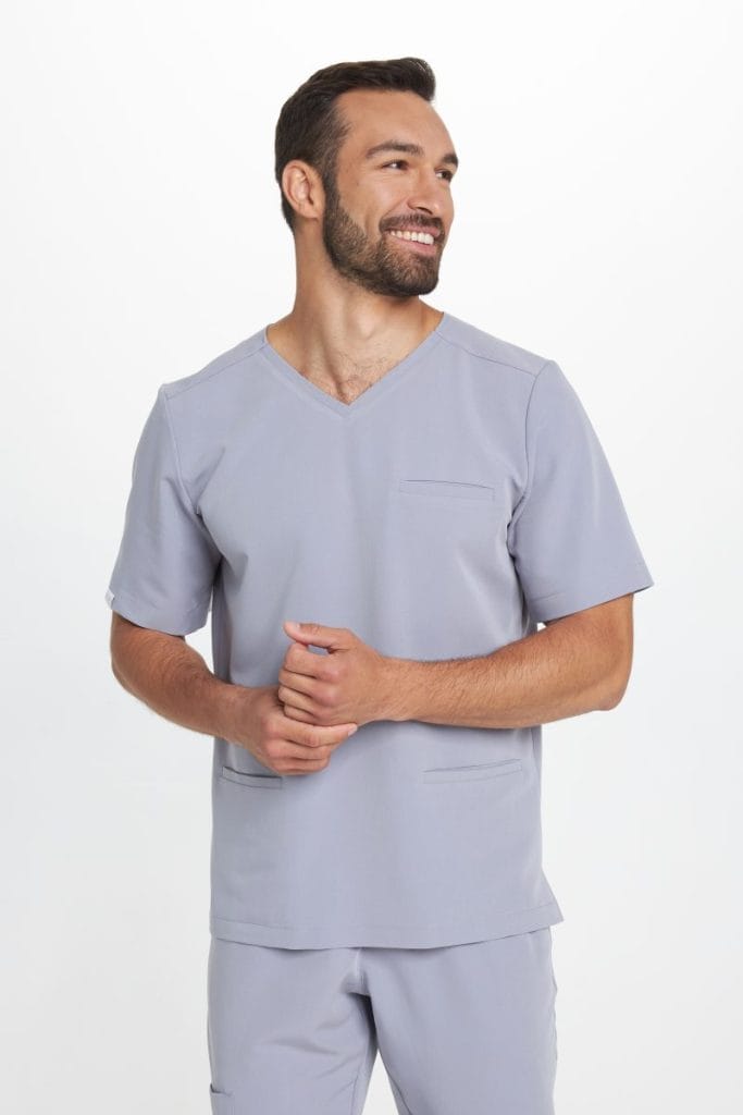 Mężczyzna w szarym uniformie medycznym z krótkim rękawem uśmiecha się.