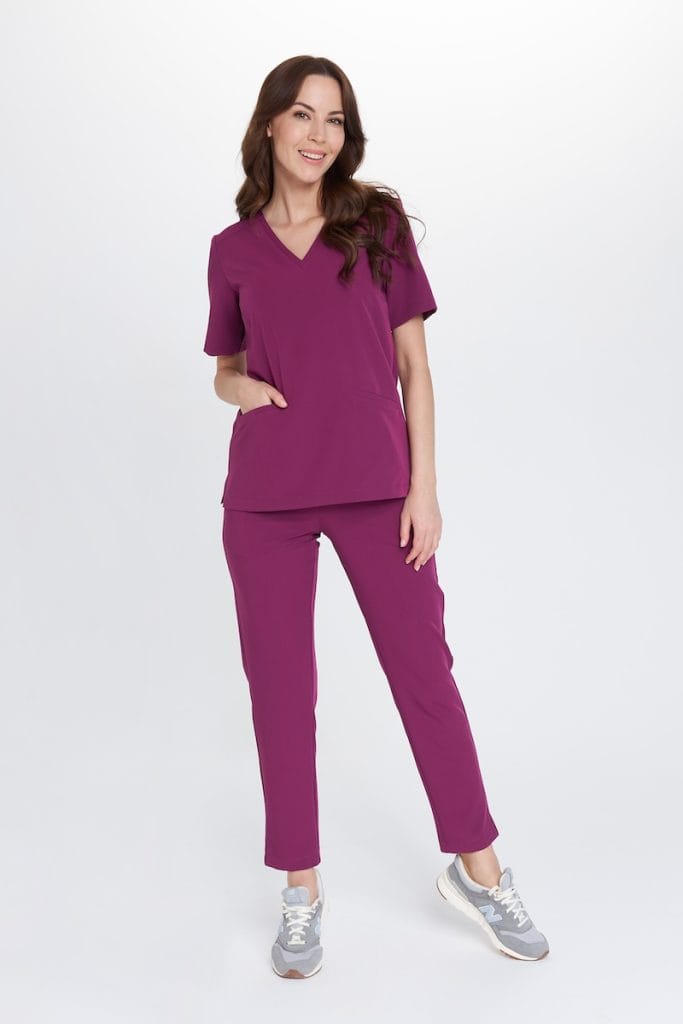 Kobieta w fioletowym medycznym komplecie scrubs Basic PLUM STAR OUTLET z kieszeniami, uśmiechnięta na białym tle