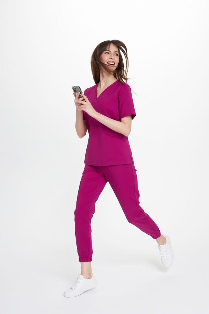 Kobieta w modnym, wygodnym medycznym komplecie w kolorze magenta trzymająca telefon.