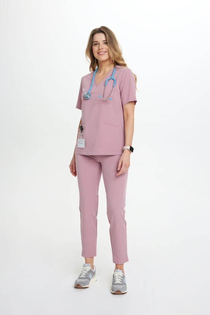 Kobieta w różowych prostych spodniach medycznych i bluzie, z niebieskim stetoskopem na szyi.