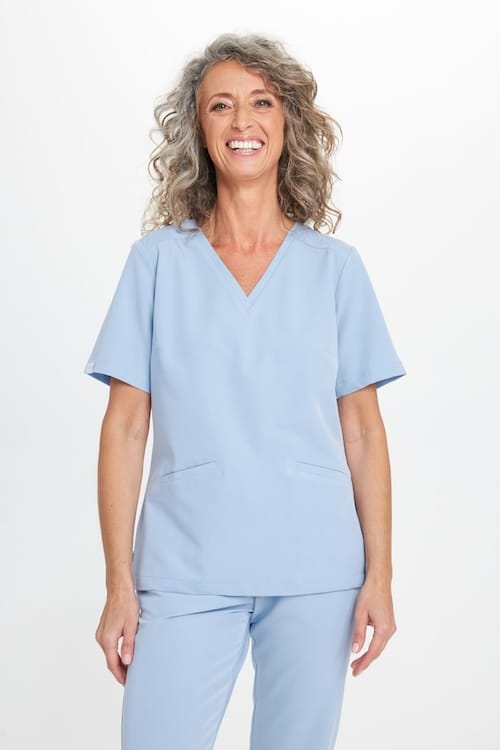 Kobieta uśmiechająca się w jasnoniebieskim stroju medycznym.