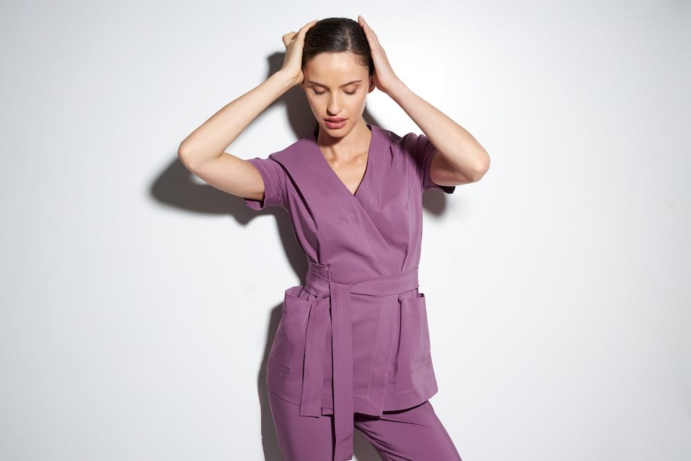 Kobieta w fioletowym komplecie odzieży medycznej z paskiem.