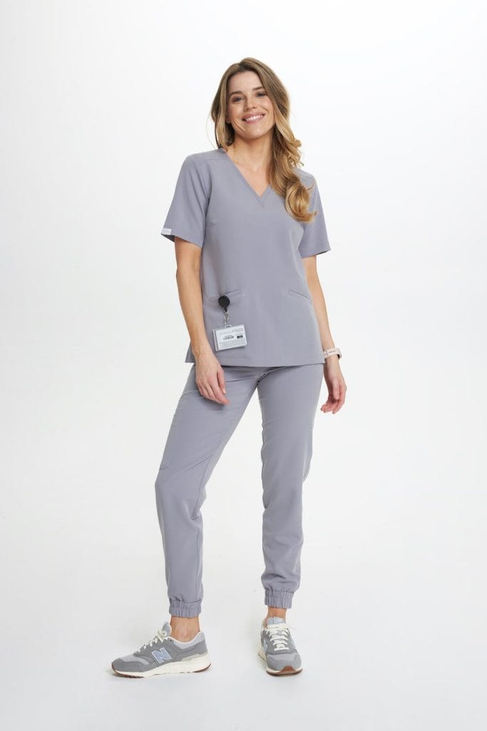 Kobieta uśmiechnięta w szarej damskiej bluzce medycznej Basic BABY SHARK i spodniach scrubs