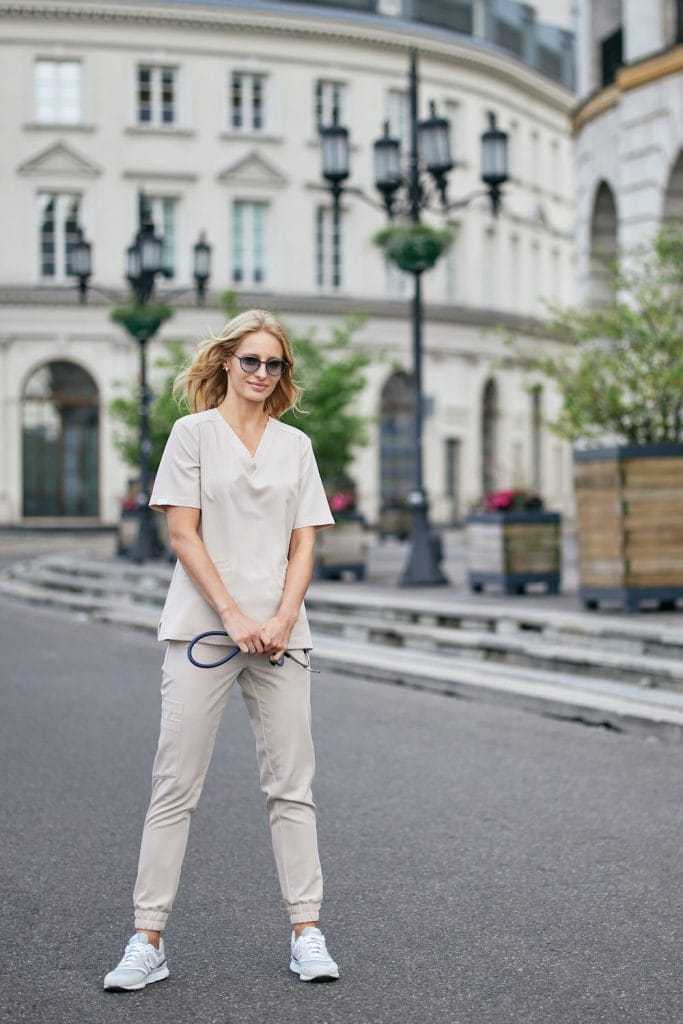 Kobieta ubrana w beżowe damskie spodnie medyczne joggery scrubs Basic COLD NUDE na tle miasta.