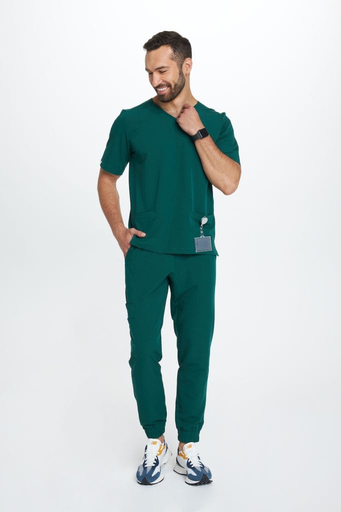 Mężczyzna w butelkowozielonych spodniach medycznych joggerach na białym tle.