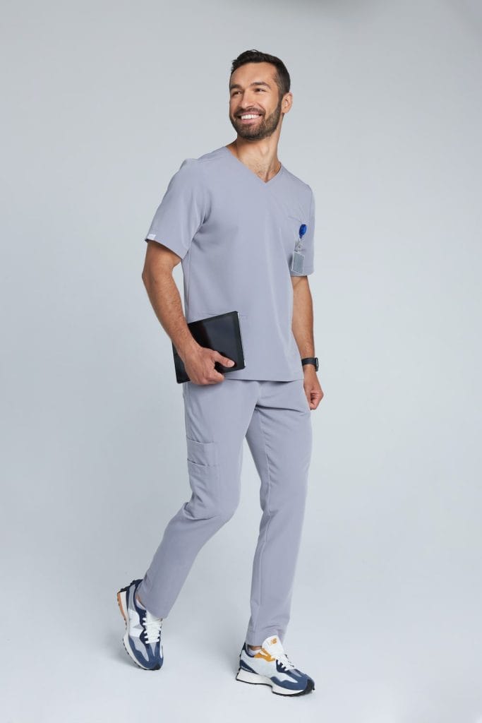 Mężczyzna w szarym medycznym komplecie scrubs trzymający tablet