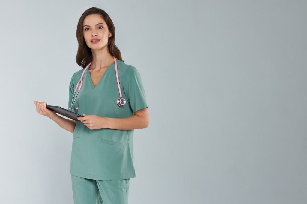 Kobieta w zielonym uniformie medycznym z różowym stetoskopem i tabletem w ręku.