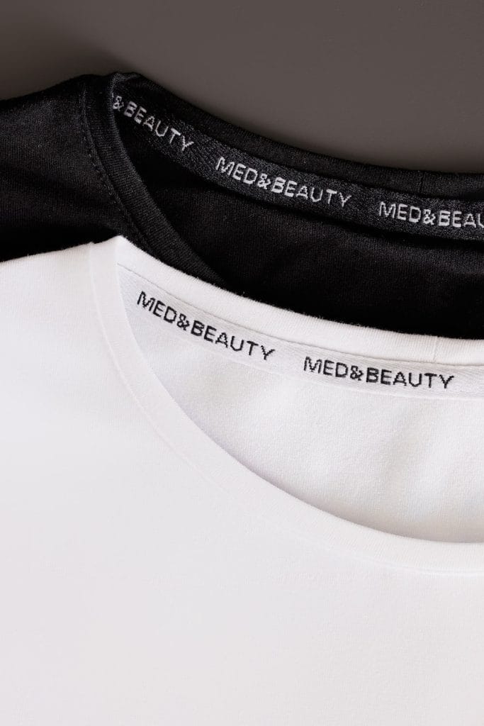 Dettaglio della scollatura della longsleeve medica da donna in bianco e nero con il logo Med&Beauty.