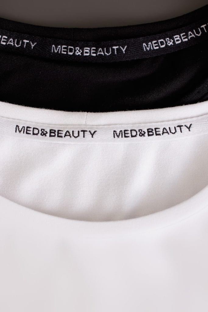Detailný záber na golier dámskeho lekárskeho dlhého rukáva v bielej farbe s logom MED&BEAUTY.