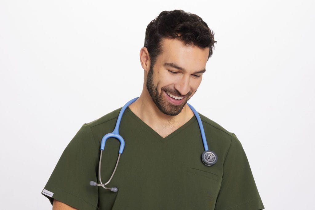 Mężczyzna w zielonym stroju medycznym ze stetoskopem uśmiecha się.