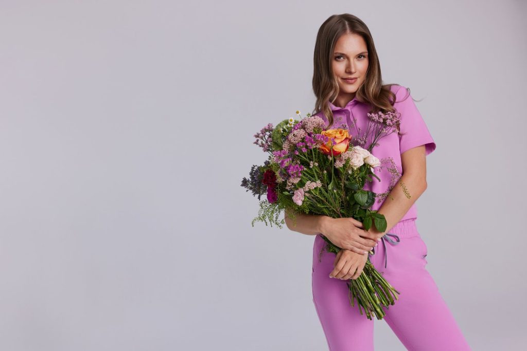 Kobieta w różowym uniformie medycznym trzyma kolorowy bukiet kwiatów.